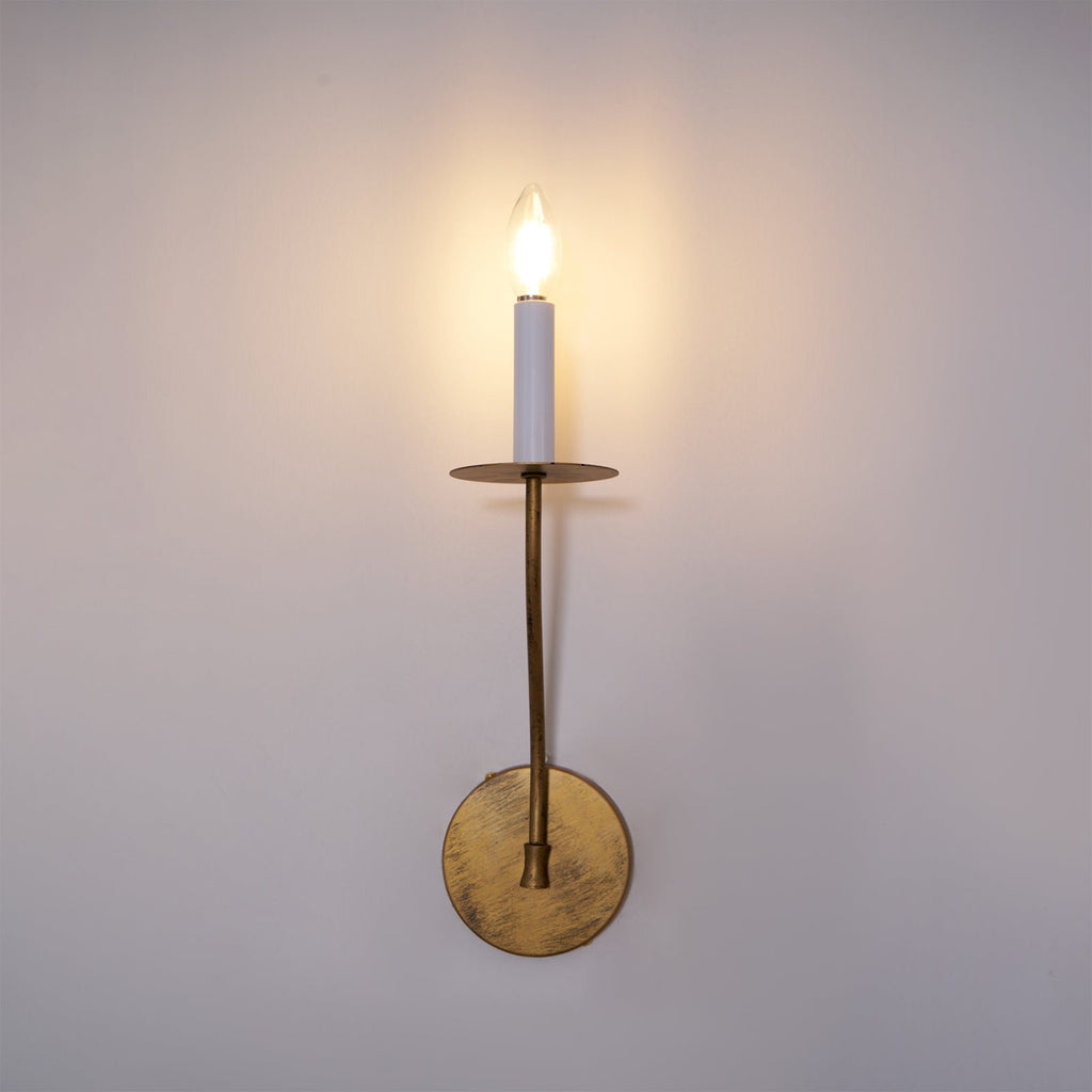 The Clérachic Eris wall lamp glows brass in close-up on a lavender-grey wall, its warm light prominent.