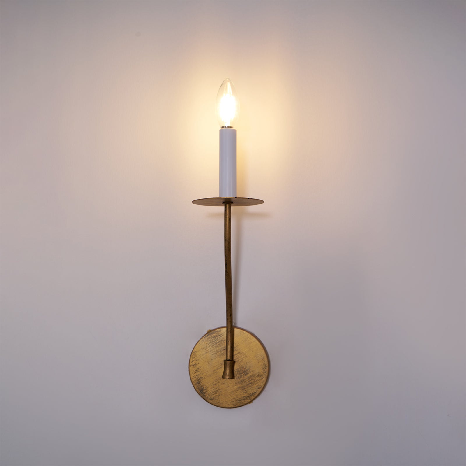 The Clérachic Eris wall lamp glows brass in close-up on a lavender-grey wall, its warm light prominent.