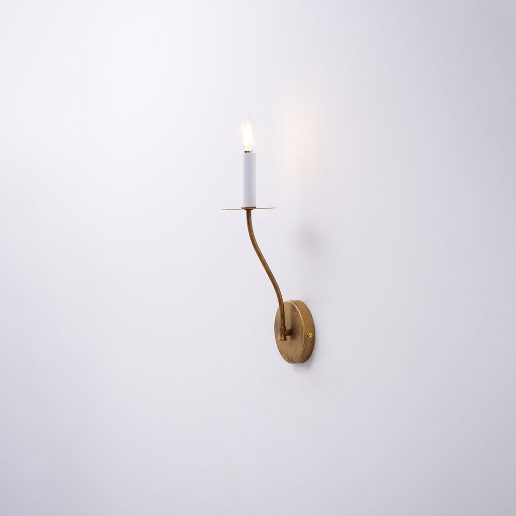 The Clérachic Eris wall lamp glows brass on a plain white wall in this close mounted shot.