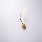 The Clérachic Eris wall lamp glows brass on a plain white wall in this close mounted shot.