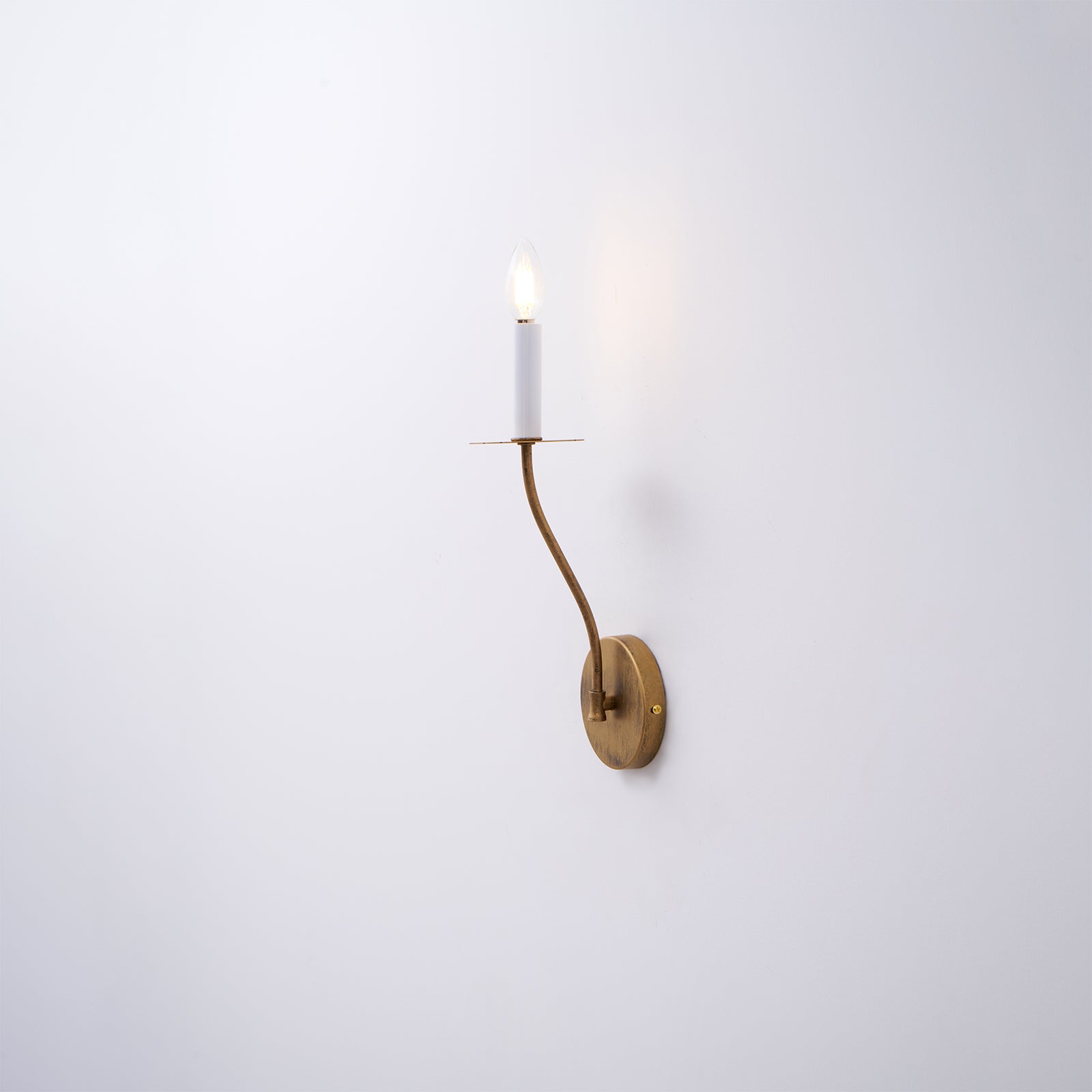 The Clérachic Eris wall lamp glows brass on a plain white wall in this close mounted shot.