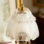 Close view of the etched floral pattern on the frosted glass shade and the brass finial on top of this Clérachic table lamp.