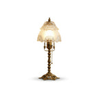 Brass table lamp with a lit frosted scalloped shade and a pull chain, with a soft shadow, on a white background, from Clérachic.
