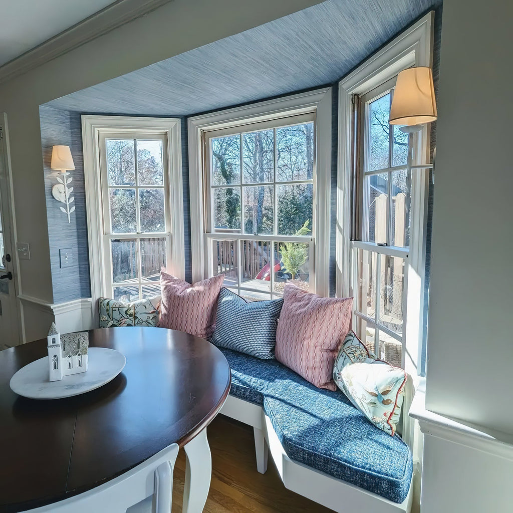 A Clérachic Evoque sconce mounted beside a bay window seat, its white shade glowing warmly at dusk.