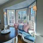 A Clérachic Evoque sconce mounted beside a bay window seat, its white shade glowing warmly at dusk.