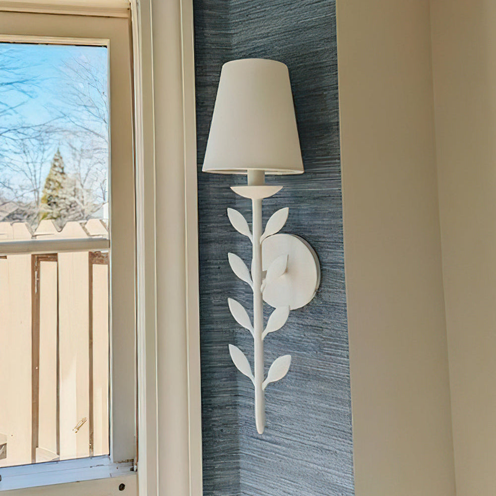 Clérachic's Evoque sconce mounted on textured wallpaper beside a window, its shade lit a soft amber.