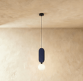 Clérachic single pendant with a navy fabric-wrapped pill panel above a milk white glass globe, on a limewashed wall.