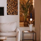 Clérachic navy-panel pendant with a white glass globe, glowing near a side table, a cream sofa and a leafy palm.