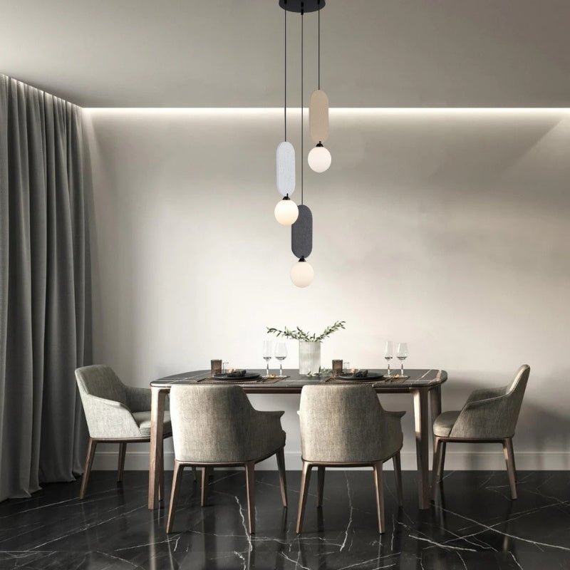 Clérachic three-head pendant in beige, grey and charcoal, hanging at varied heights over a dark dining table with grey chairs.