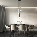 Clérachic three-head pendant in beige, grey and charcoal, hanging at varied heights over a dark dining table with grey chairs.