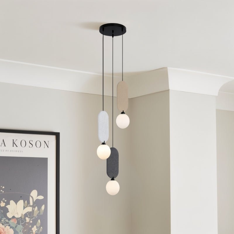 Clérachic three-head pendant with fabric panels and white globes, hung in a pale room corner beside a framed floral print.
