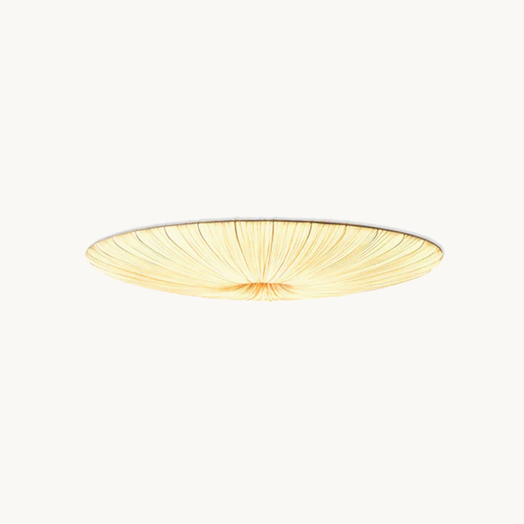 This Clérachic flush ceiling light on a plain backdrop: a wide, shallow beige fabric shade with fine pleats gathered to the centre and lit warm.