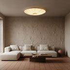 Lit Clérachic fabric ceiling light above a low cream sofa and a rough wooden coffee table, in a room with textured plaster walls.