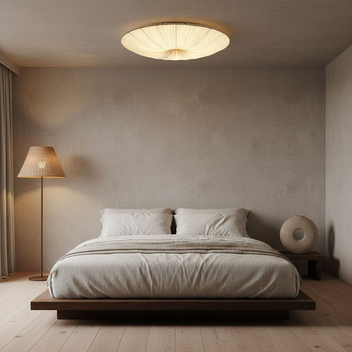 Clérachic pleated ceiling light glowing over a low platform bed, with a woven floor lamp and a round vase beside it.