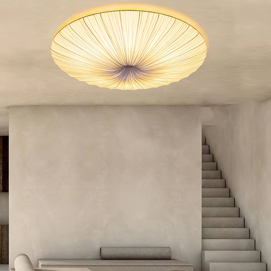 Looking up at a Clérachic pleated ceiling light, its folds radiating from the centre, with a plaster wall and open staircase below.
