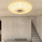 Looking up at a Clérachic pleated ceiling light, its folds radiating from the centre, with a plaster wall and open staircase below.