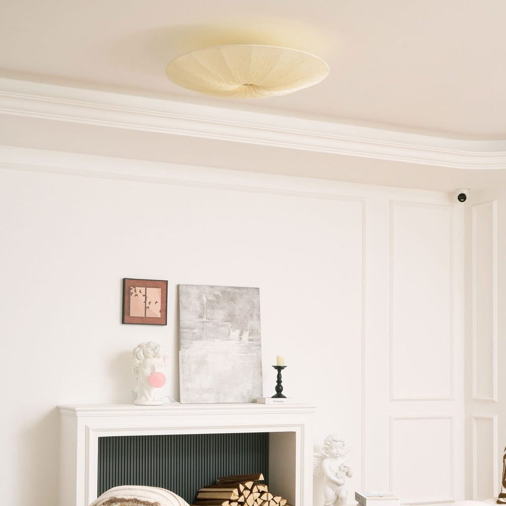The same Clérachic fabric ceiling light seen unlit above a white mantel with logs, a plaster bust and framed art.