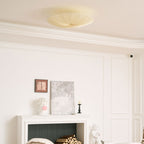 The same Clérachic fabric ceiling light seen unlit above a white mantel with logs, a plaster bust and framed art.