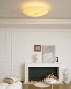 Clérachic pleated ceiling light lit with a soft halo on the ceiling, above a white mantel with logs and framed artwork.