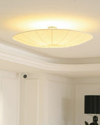 A Clérachic pleated shade on a short central stem, glowing with a halo on a coffered ceiling above white panelling.