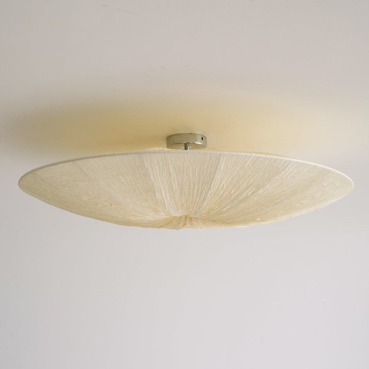 Underside of a Clérachic fabric ceiling light on a small metal canopy, with soft cream pleats and a pale ceiling.