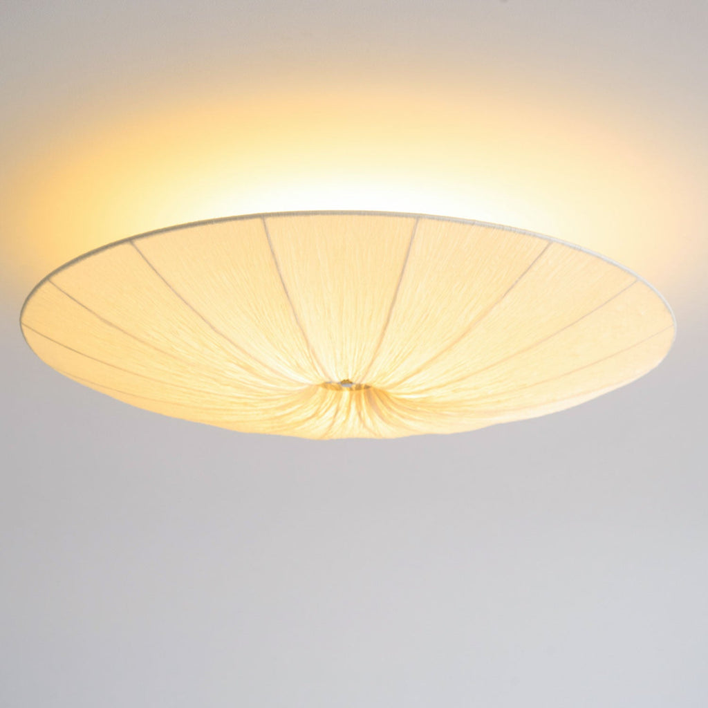 Clérachic pleated ceiling light lit with a bright halo, its gathered centre and wide rim seen from below.