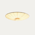 Clérachic fabric ceiling light on a pale grey backdrop, tilted slightly and lit, with the pleats gathered to the centre.