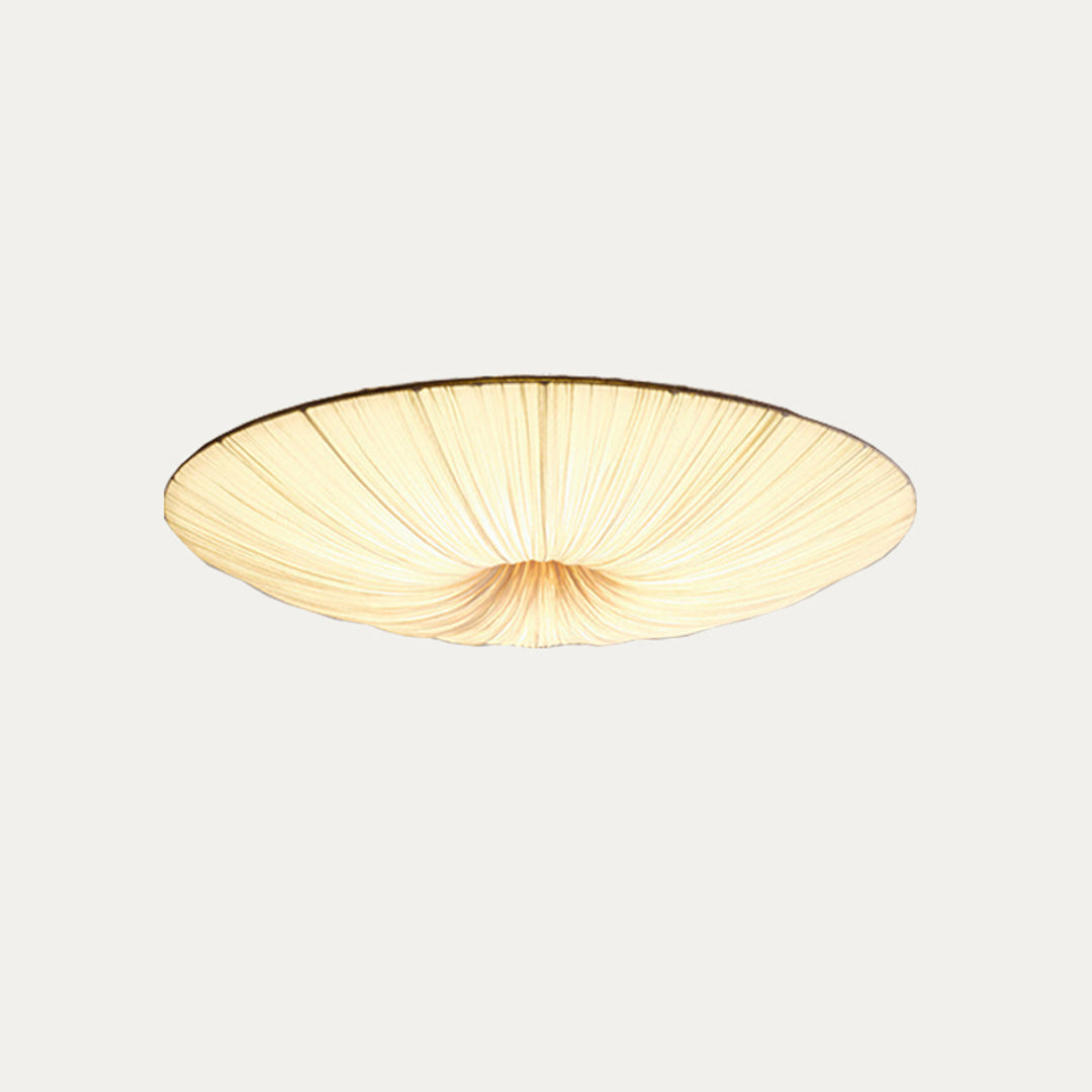 Clérachic fabric ceiling light on a pale grey backdrop, tilted slightly and lit, with the pleats gathered to the centre.