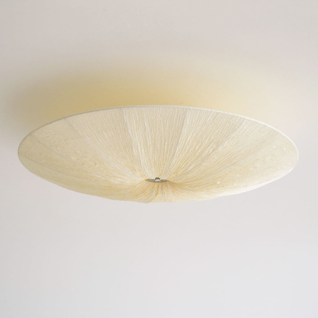 Unlit Clérachic fabric ceiling light seen from below, with a cream textured shade and a small metal canopy on a white ceiling.