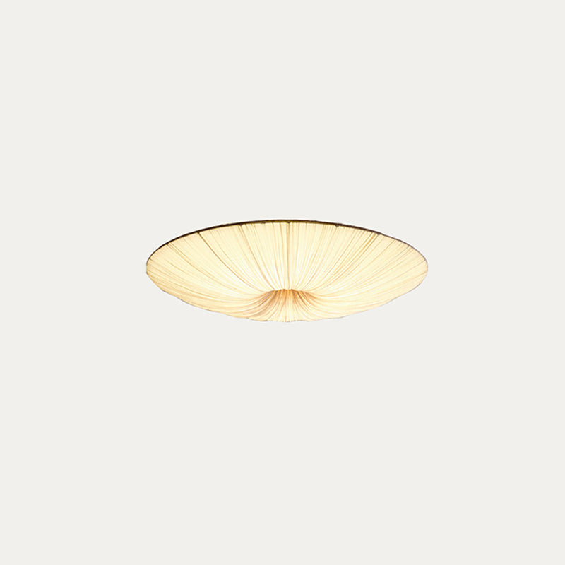 Small Clérachic pleated ceiling light on a pale grey backdrop, lit warm with a dark rim line.