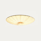 Mid-sized Clérachic pleated ceiling light on a pale grey backdrop, lit, with the fabric drawn in towards the middle.