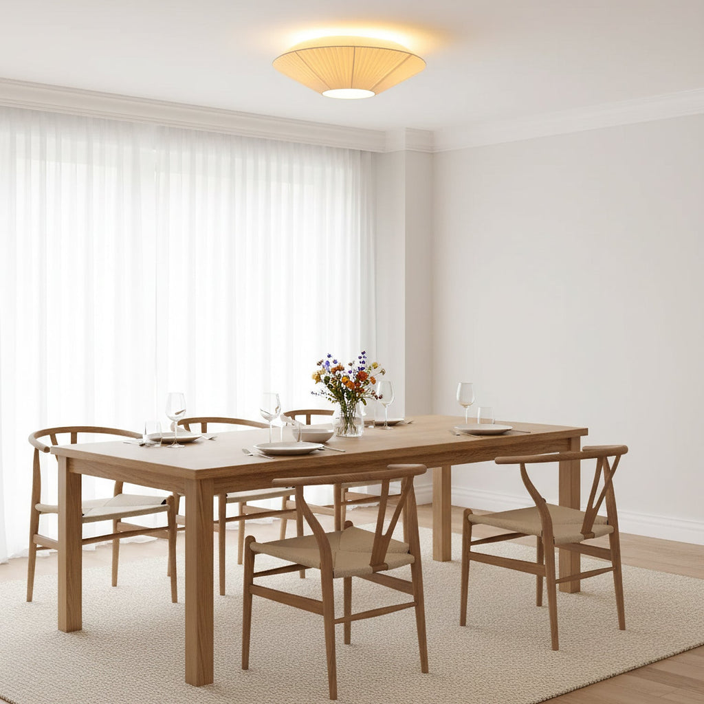 A Clérachic pleated ceiling light casting warm light over a pale room with a long oak dining table and woven-seat chairs.