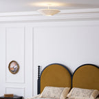 Clérachic pleated ceiling light on a short rod above a white panelled wall, beside a bed with an arched mustard headboard.