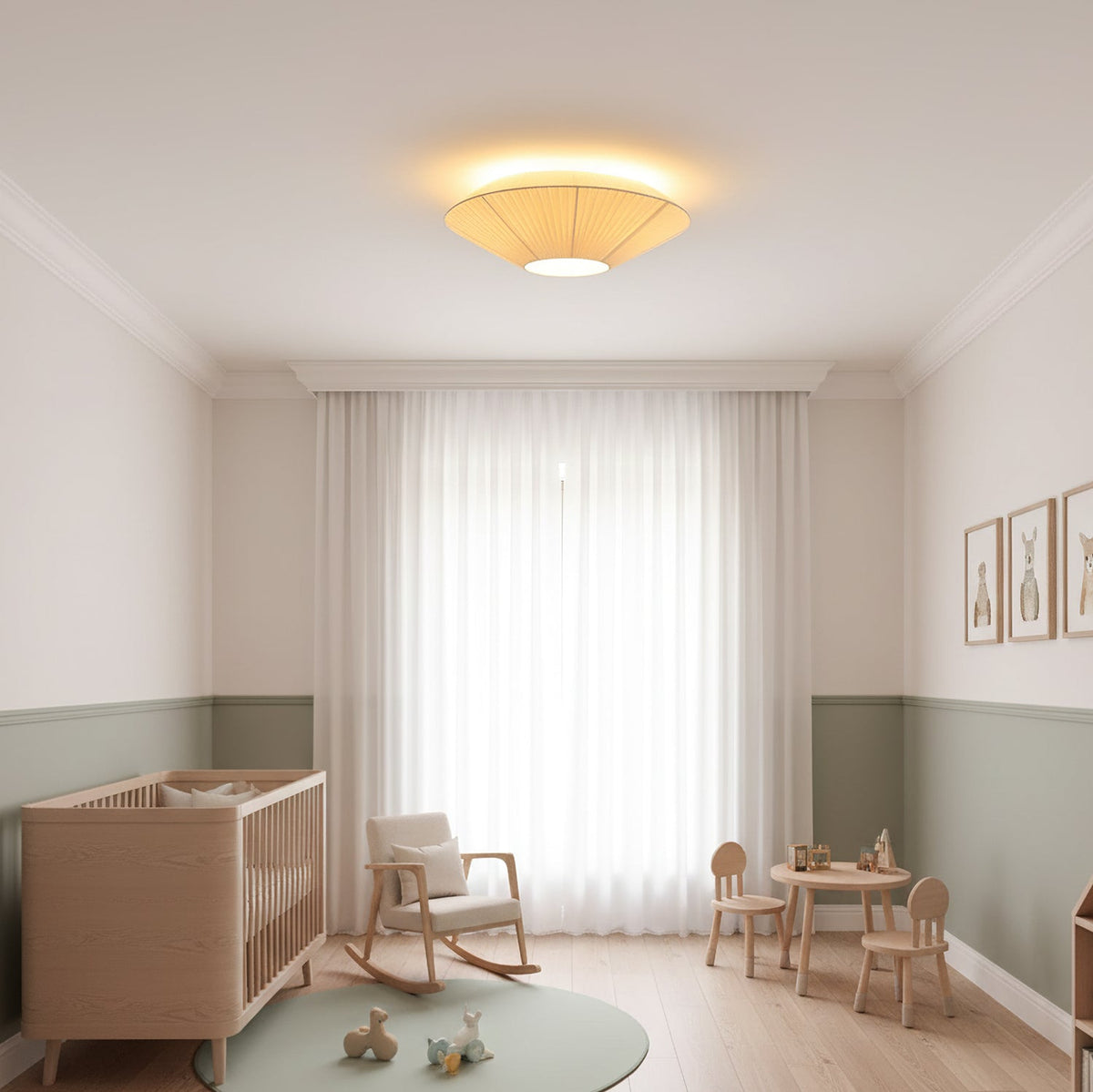 A Clérachic pleated ceiling light lit above a nursery with a wooden cot, a rocking chair, a small table and sheer curtains.
