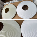 Two flat, ribbed white fabric shade discs with centre holes laid on a table, with a close view of the fine pleats on this Clérachic ceiling light.