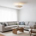 Clérachic pleated ceiling light hanging on a short stem above a grey corner sofa, a wooden coffee table and a woven rug.