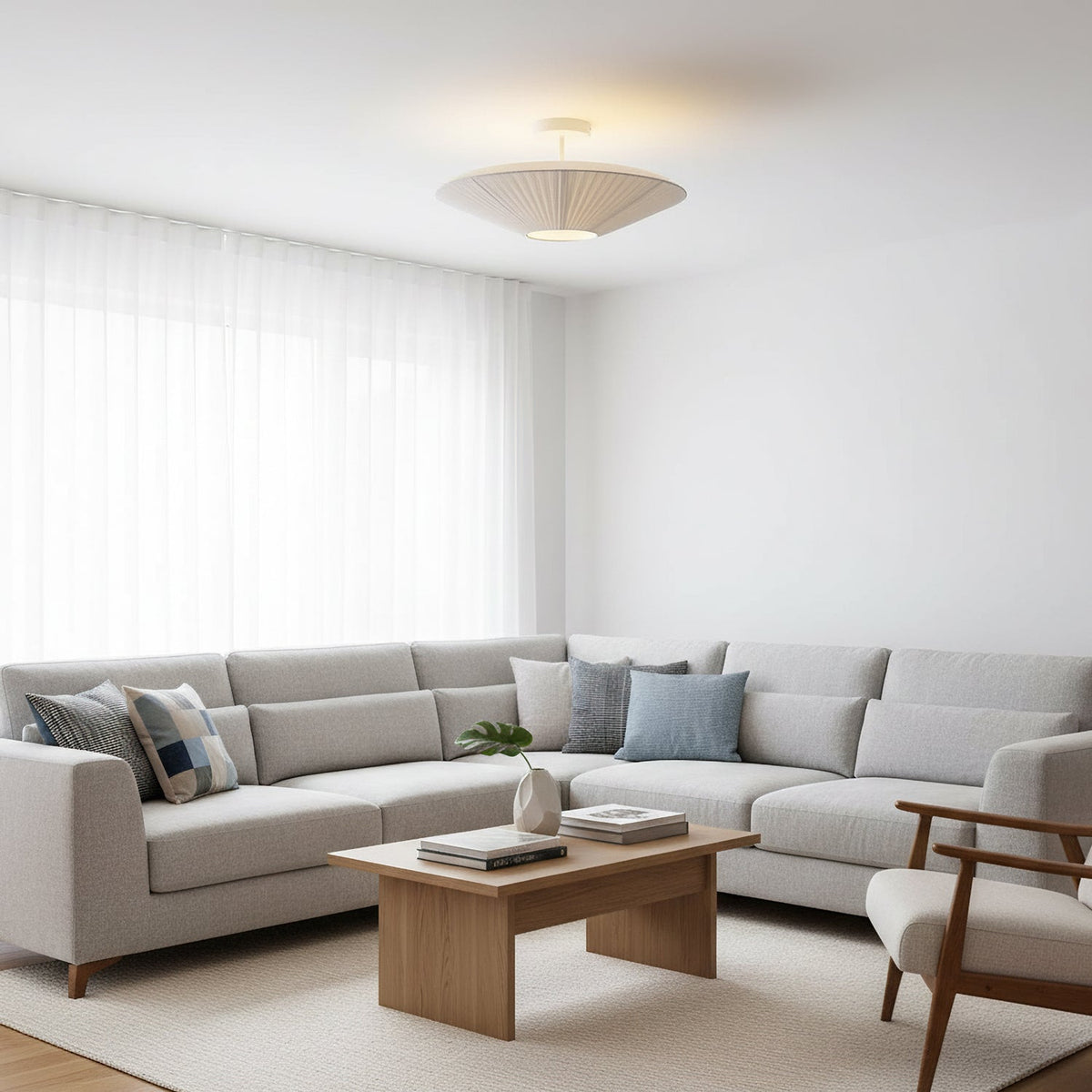 Clérachic pleated ceiling light hanging on a short stem above a grey corner sofa, a wooden coffee table and a woven rug.