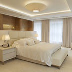 A Clérachic ivory pleated ceiling light set into a recessed ceiling above a cream bed, with lit bedside lamps and long curtains.