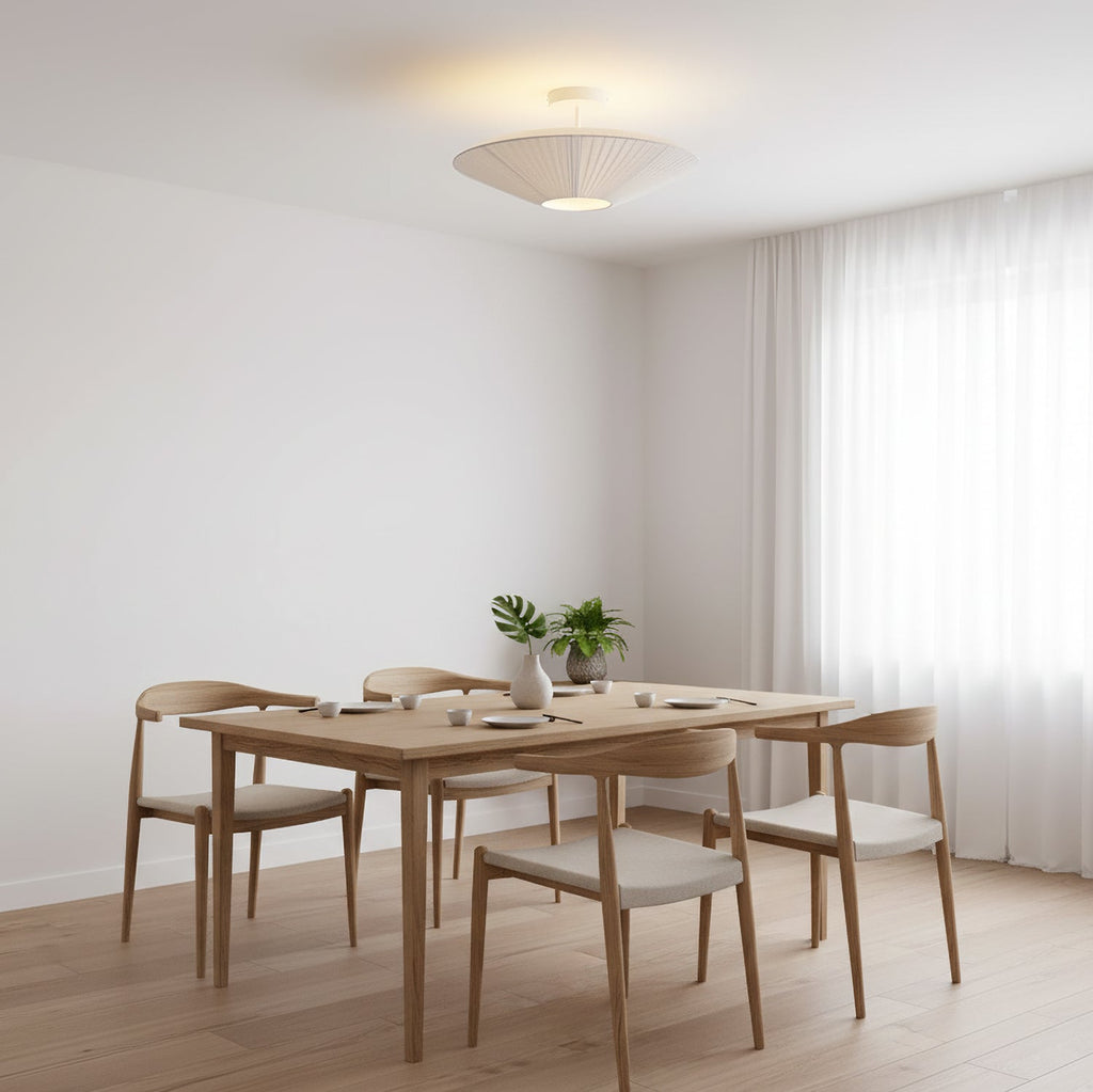Clérachic pleated ceiling light on a short stem above a light wood dining table with four chairs, in a white room with sheer curtains.
