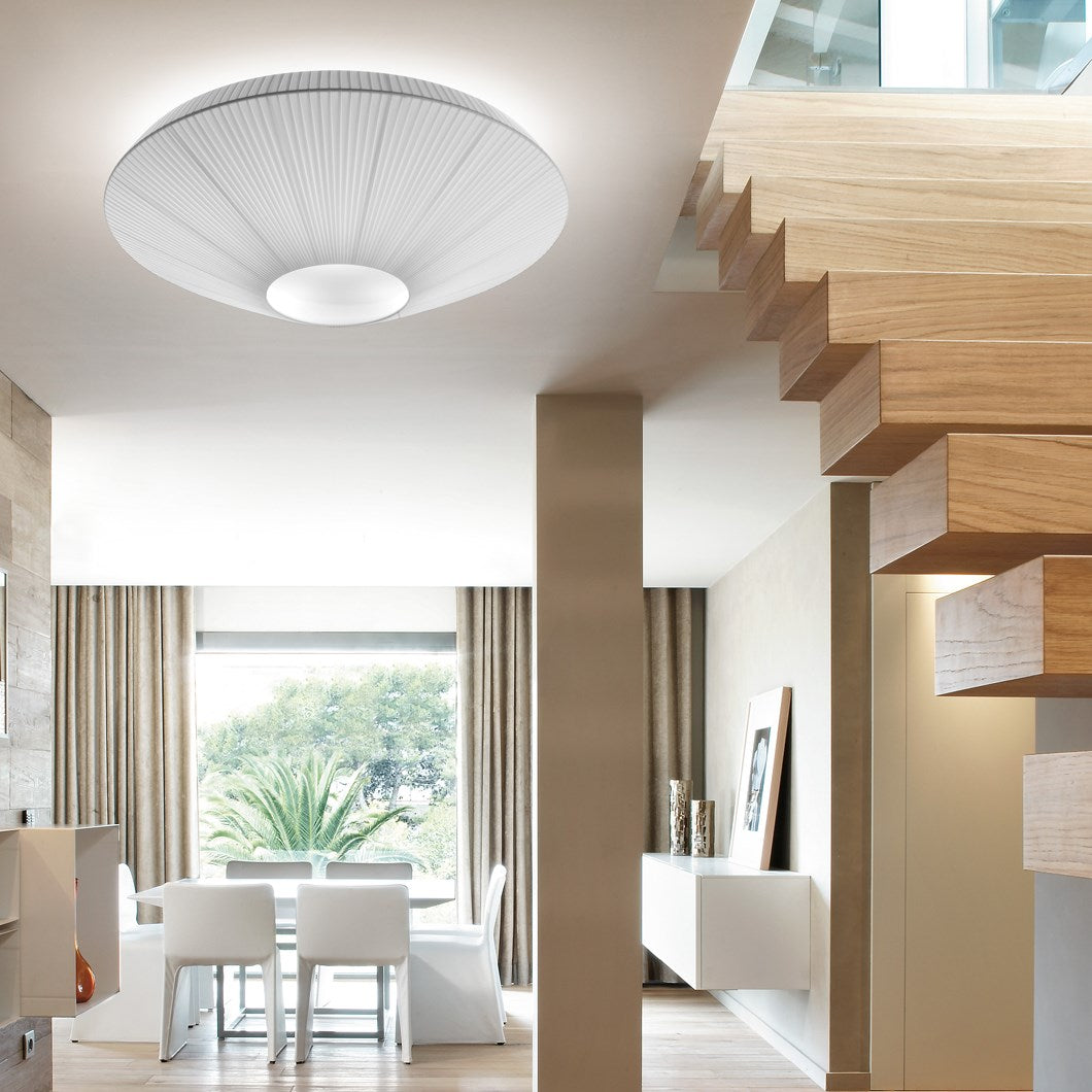 Large white Clérachic pleated ceiling light above a stairwell with floating wooden steps and a dining area in the distance.