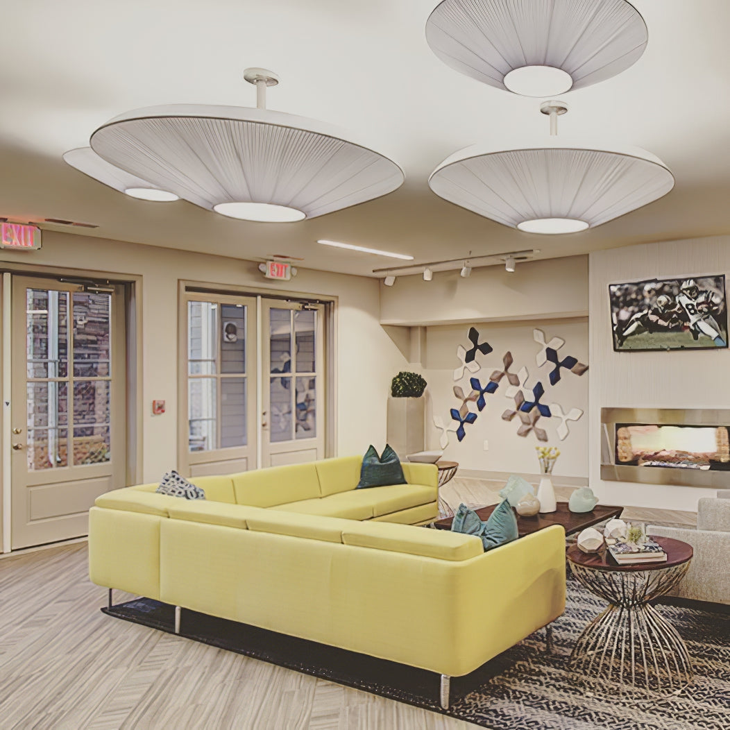 Three large Clérachic pleated ceiling lights in white, hung at different heights above a yellow sectional sofa in a lounge.