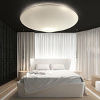 Big white Clérachic pleated ceiling light over a bed with white curtains drawn behind it, in a room with a dark ceiling.
