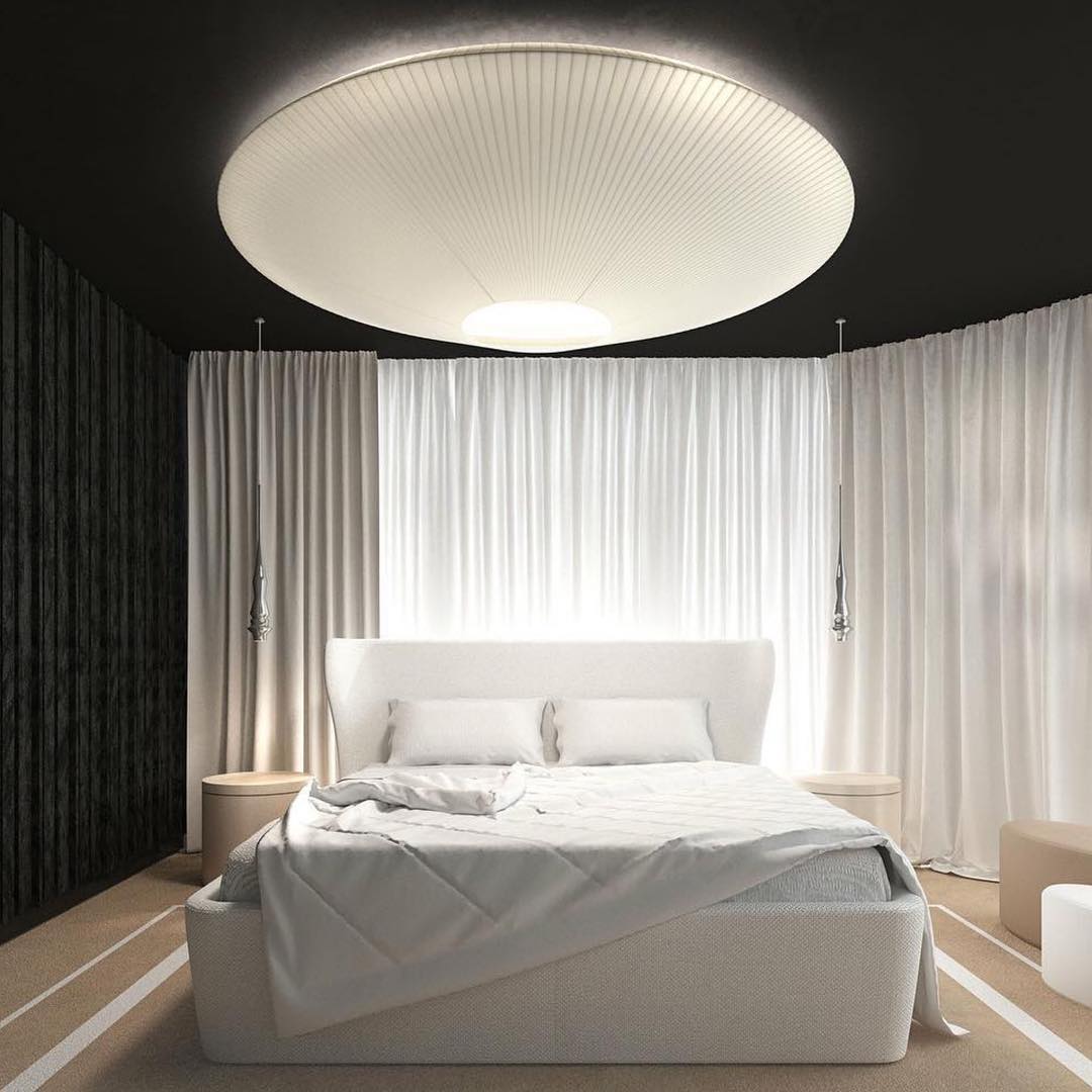 Big white Clérachic pleated ceiling light over a bed with white curtains drawn behind it, in a room with a dark ceiling.