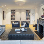 Clérachic pleated ceiling light above a living room with two navy armchairs, a dark coffee table and built-in bookshelves.