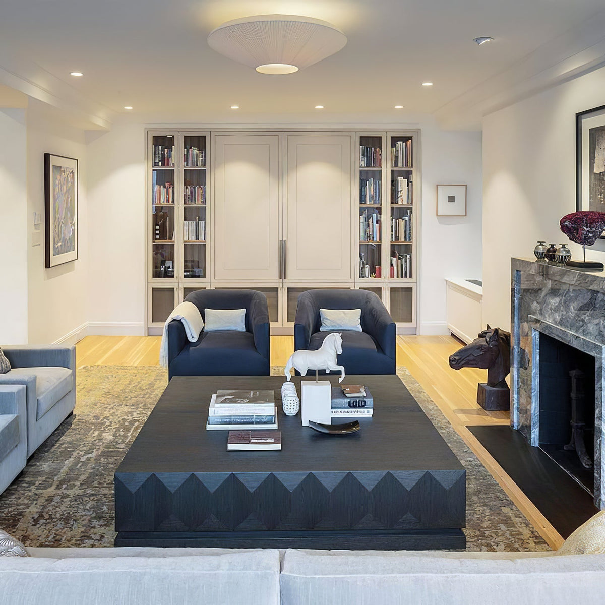 Clérachic pleated ceiling light above a living room with two navy armchairs, a dark coffee table and built-in bookshelves.