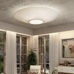 Wide ivory Clérachic pleated ceiling light on a rough concrete ceiling, with tall French doors and long sheer curtains below.
