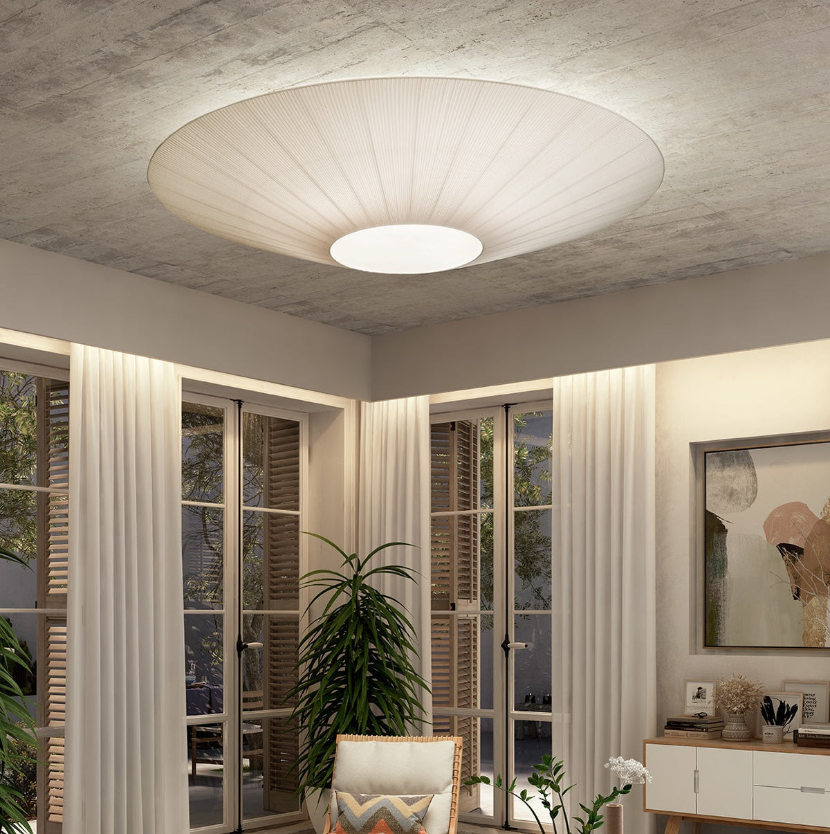 Wide ivory Clérachic pleated ceiling light on a rough concrete ceiling, with tall French doors and long sheer curtains below.