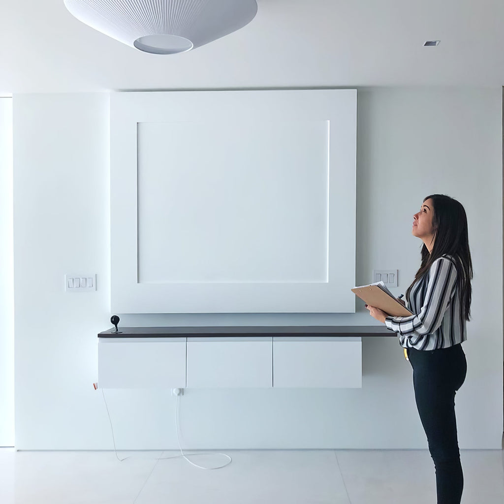 A woman looking up at a white Clérachic pleated ceiling light in a bright room with a built-in white wall unit.