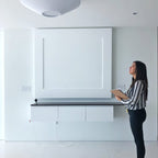 A woman looking up at a white Clérachic pleated ceiling light in a bright room with a built-in white wall unit.