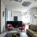 Several grey-toned Clérachic pleated ceiling lights across a high ceiling above an open-plan lounge with pink armchairs.